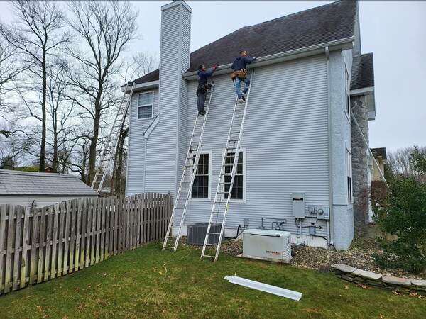 Two gutter installers on extension ladders installing seamless gutters along a South Jersey home